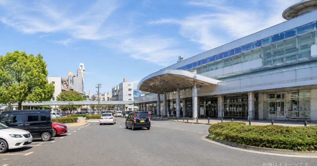松江駅の改札前と駅直結施設へ向かう動線を背景に、喫煙場所を探す旅行者が案内表示を確認している様子